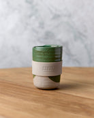 Green travel mug with beige band, close view on timber
