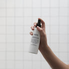 A hand spraying the 200 ml white Lemongrass & Lime room spray bottle against white tiles.