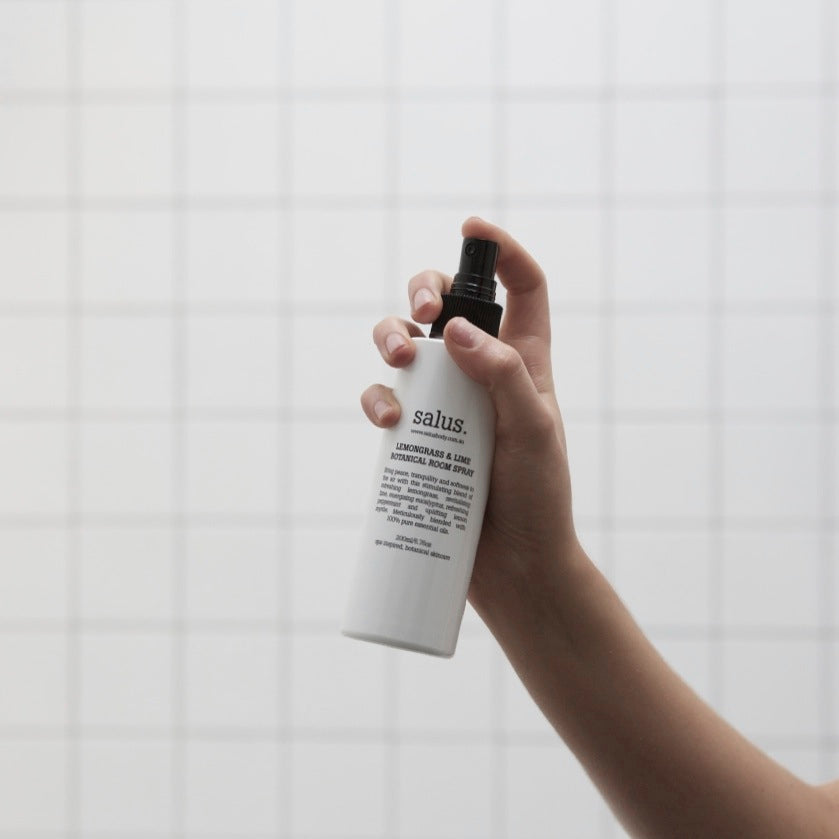 A hand spraying the 200 ml white Lemongrass & Lime room spray bottle against white tiles.