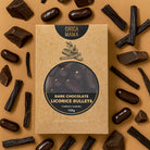 Licorice bullets box on tan among dark chocolate chunks, licorice root sticks and loose bullets