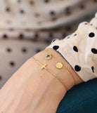 Model's wrist wearing the cross bracelet layered with other fine gold chains