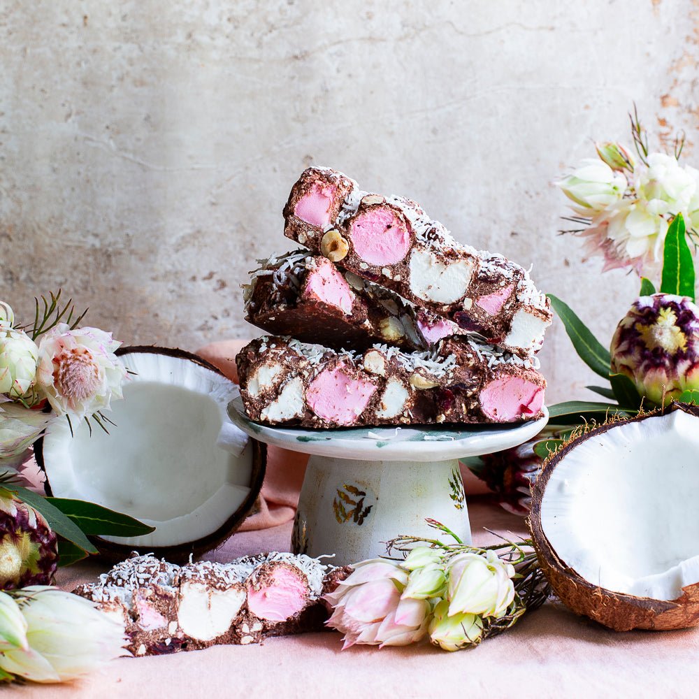Signature Recipe rocky road piled on a cake stand with a halved coconut, hazelnuts and marshmallows