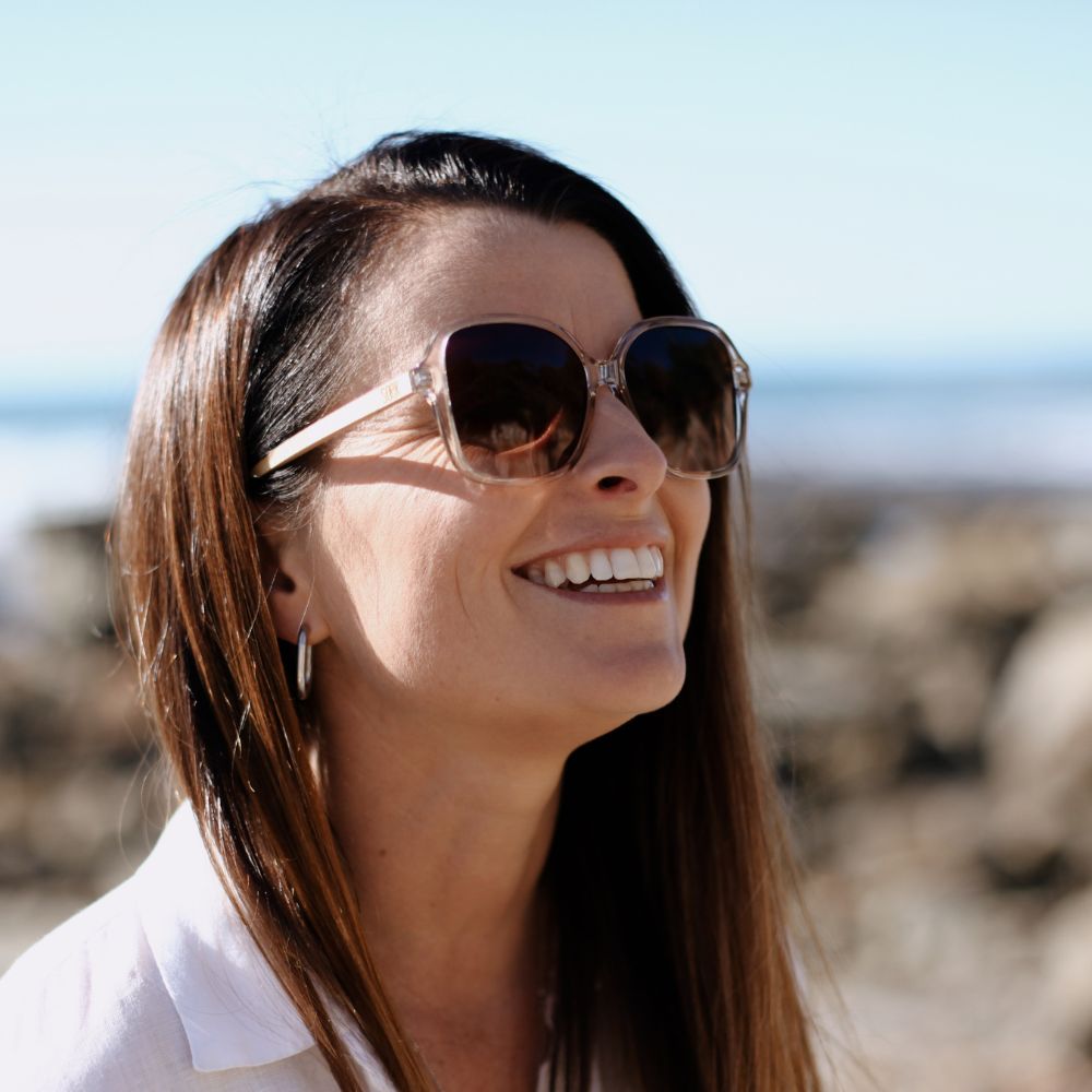 Model laughing on a rocky beach wearing the Scarlett champagne sunglasses