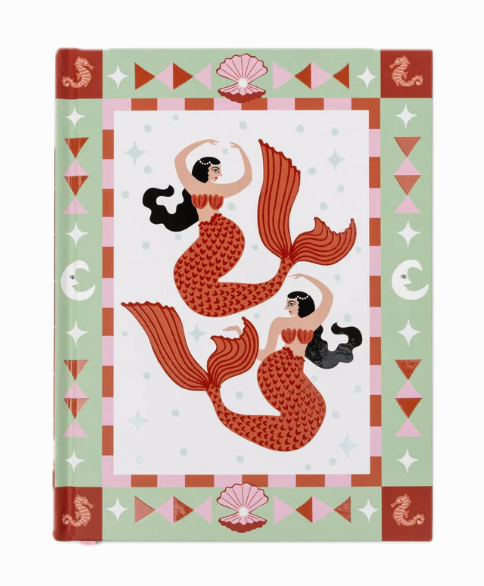 A Dopo journal with two red mermaids inside a sage green border of shells and moons