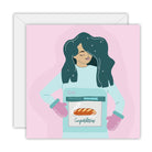 Square pink card with a woman in oven mitts holding an oven with a bun inside, lettered Congratulations, on a white envelope