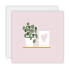 Square pale pink card with a potted plant on a gold shelf beside a framed pink heart lettered home, on a white envelope