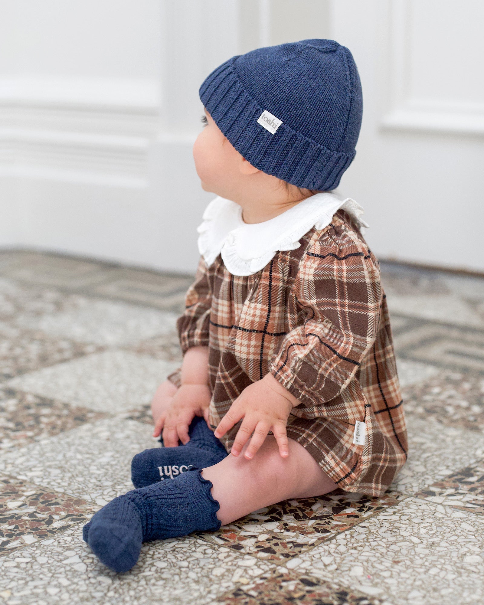 Baby wearing the navy Rover beanie with a brown check romper and navy Toshi socks