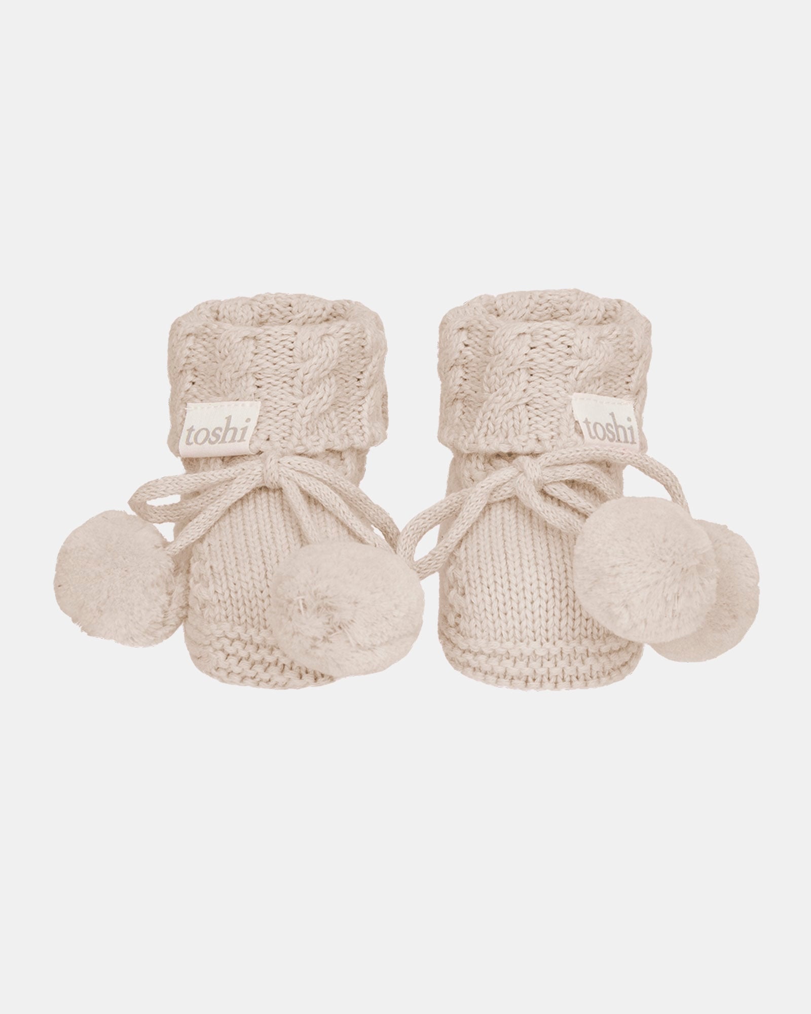 A pair of Toshi Organic Booties Yummy in oatmeal cable knit with tie fastenings and pompoms