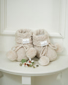 The oatmeal booties on a white side table beside a spray of small white blossom