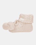 Side view of a single oatmeal bootie showing the cable-knit cuff, garter-stitch foot and pompom ties