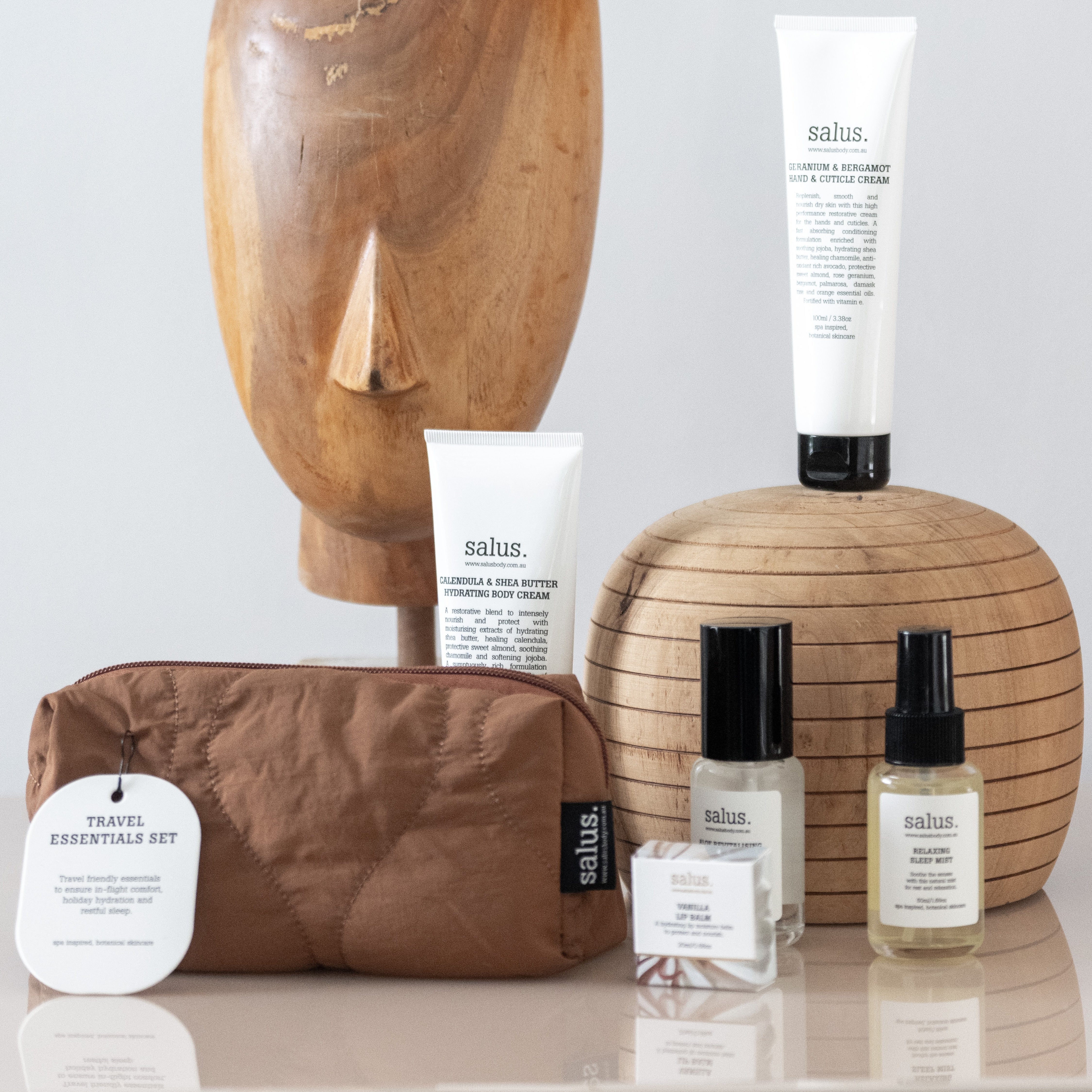 Salus Travel Essentials Set styled with a carved timber head, creams, mists and the tan travel bag