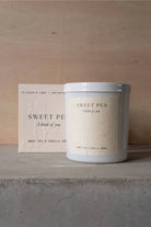 The Sweet Pea candle in its white vessel beside its cream box.
