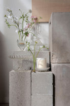 The Sweet Pea candle on stacked concrete blocks among sweet pea stems.