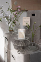 The Sweet Pea candle on a glass stand, with its box and sweet peas behind.