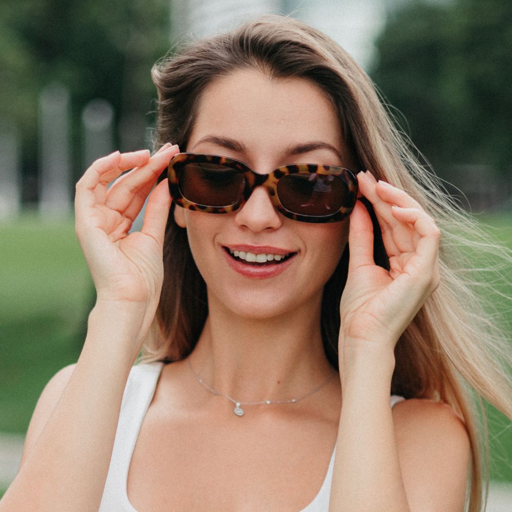A woman outdoors in a park wearing the Vibe sunglasses
