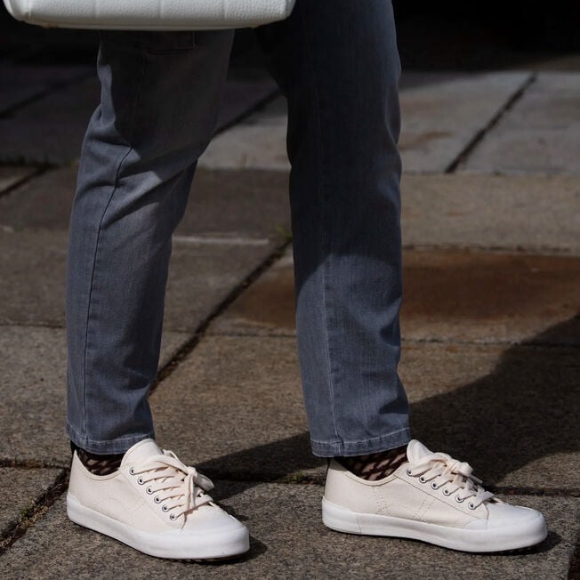 Legs mid-stride in cream Hosier sneakers with leopard-print socks and grey jeans