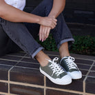 Woman seated on brick steps wearing dark olive Hosier sneakers with cuffed jeans