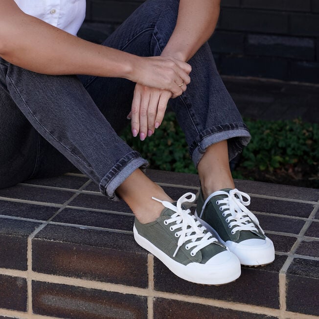 Woman seated on brick steps wearing dark olive Hosier sneakers with cuffed jeans