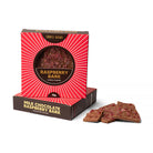 Red sunburst box of milk chocolate raspberry bark standing on a second box, with shards of raspberry-studded bark beside it