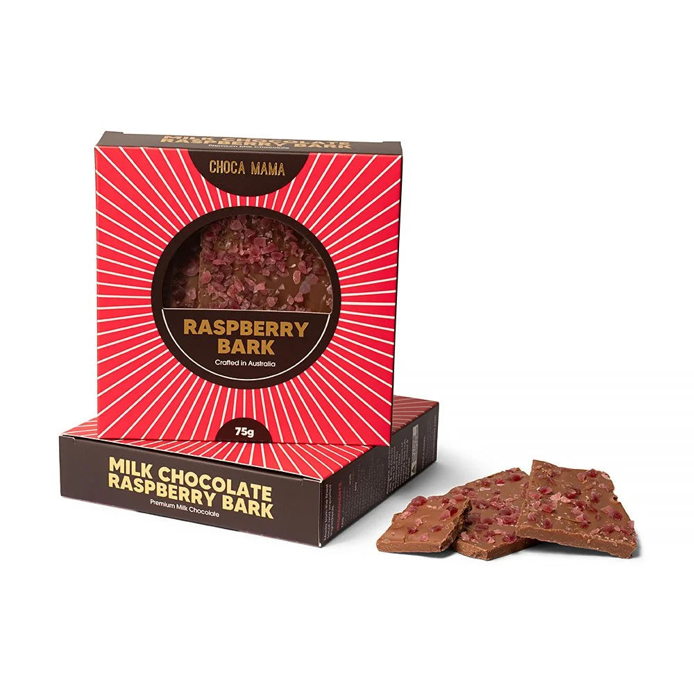 Red sunburst box of milk chocolate raspberry bark standing on a second box, with shards of raspberry-studded bark beside it