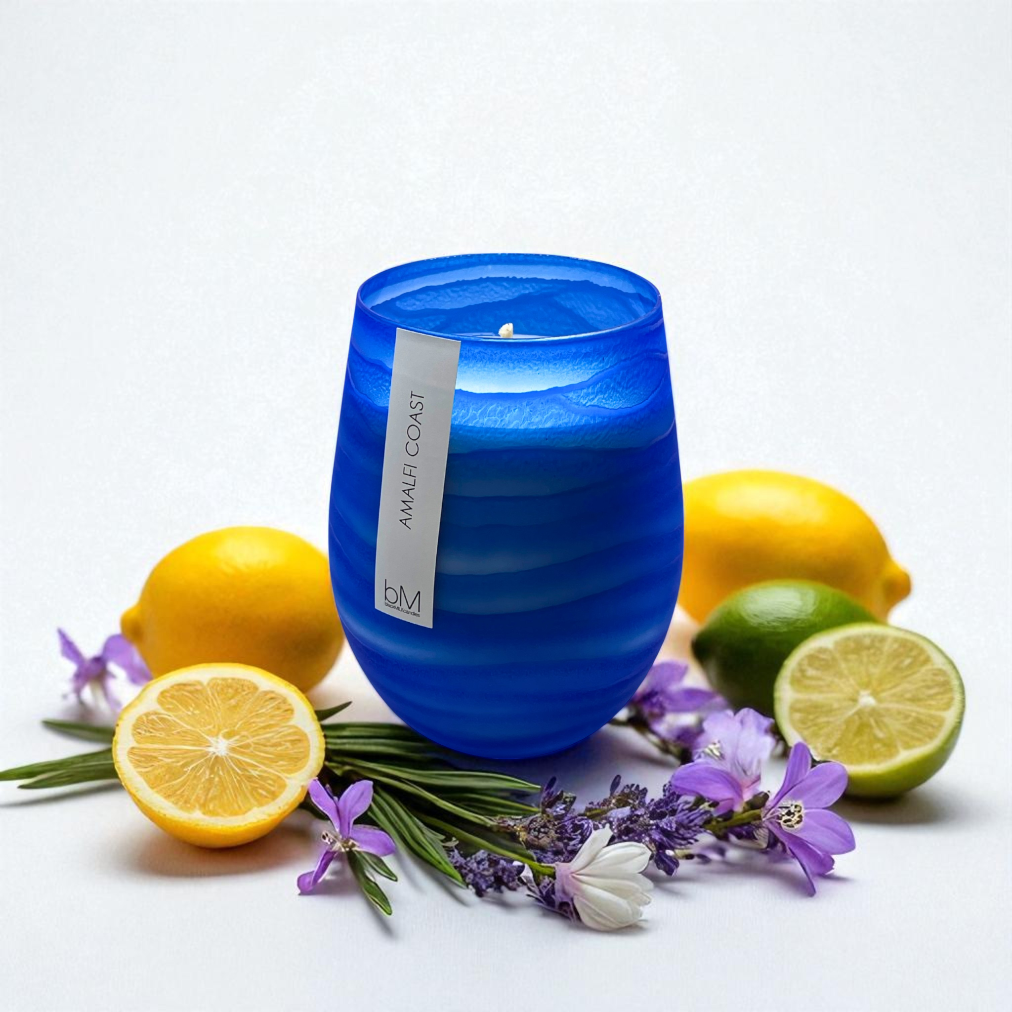Wave Blue Amalfi Coast candle surrounded by whole and halved lemons, limes, lavender and freesia — the fragrance notes