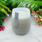 Wave White Beachside candle on pale sand with tropical foliage and coral flowers behind