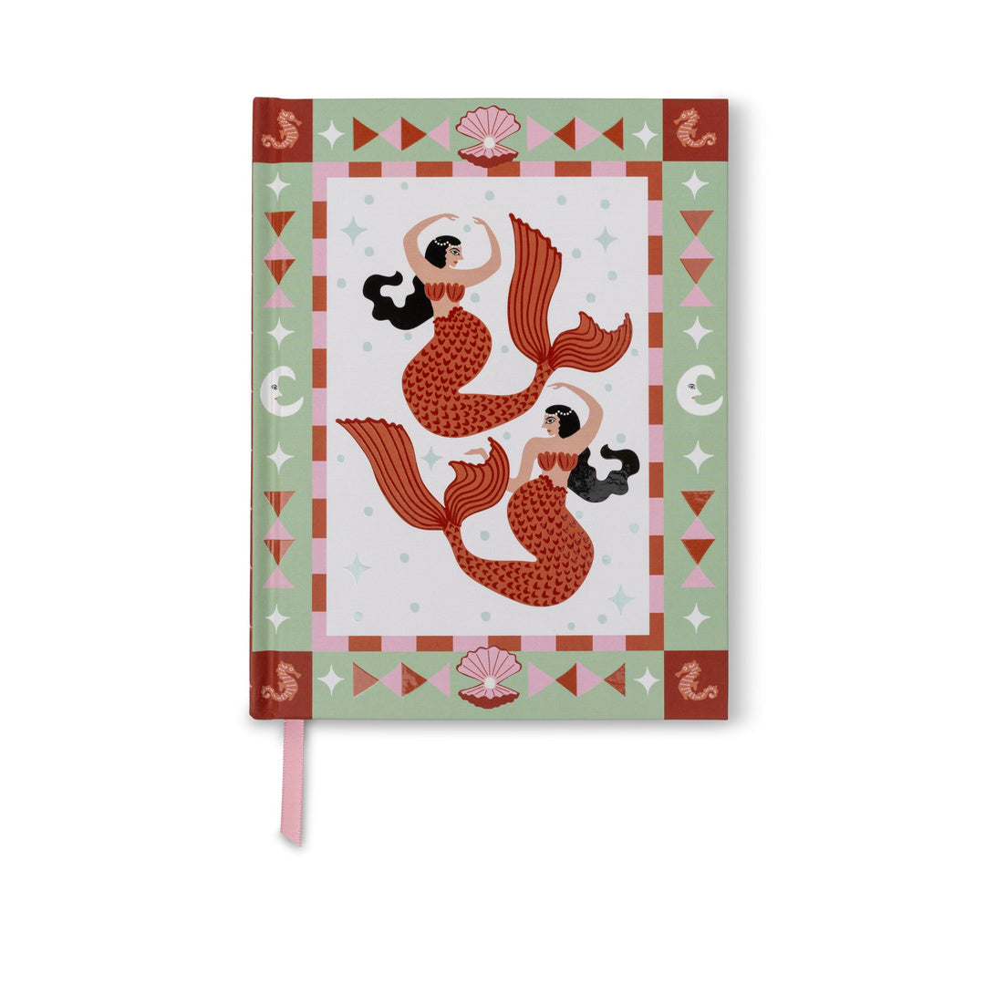 A Dopo journal standing upright, its cover showing two red mermaids inside a sage green border of shells, seahorses and moons, with a pink ribbon marker hanging below