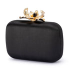 Black satin clutch turned to a three-quarter view, the gold orchid clasp on top