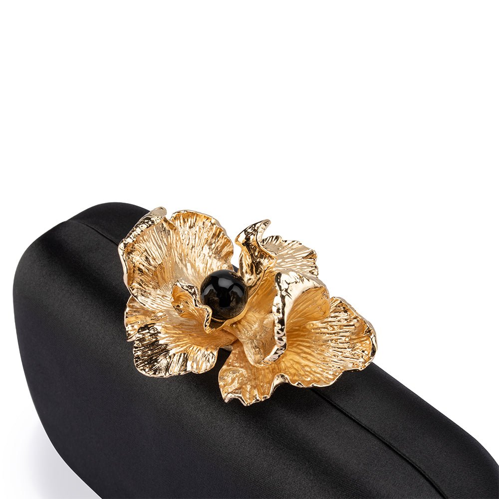 Gold orchid clasp with a black bead centre, seen from above on the black satin lid