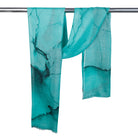 The Aqua Mirage scarf hanging over a rail, showing the dark ink-like veining and fringed ends