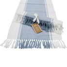 Chambray Blue and white table runner laid flat with blue and white tassels, a second runner rolled and tied with a ribbon on top