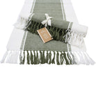 Olive green and white table runner laid flat with olive and white tassels, a second runner rolled and tied with a ribbon on top