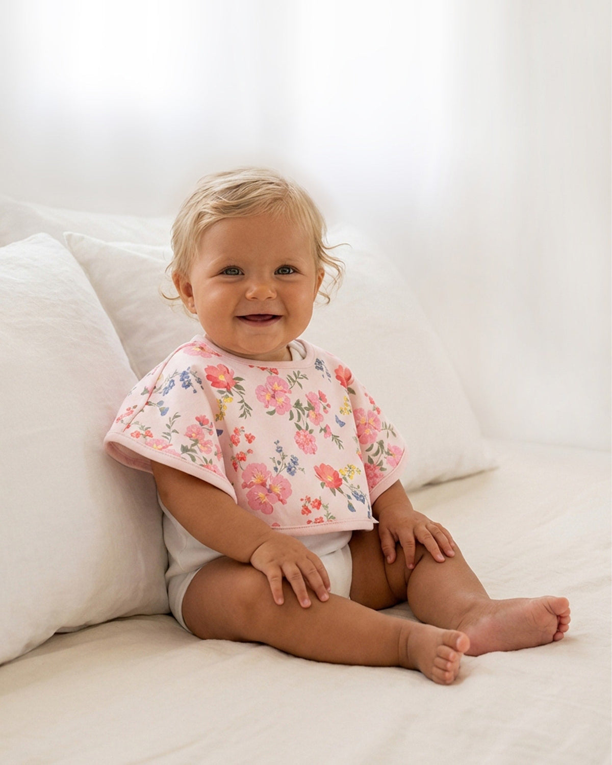 Smiling baby sitting on a bed wearing the Wild Garden cloth over the shoulders like a bib
