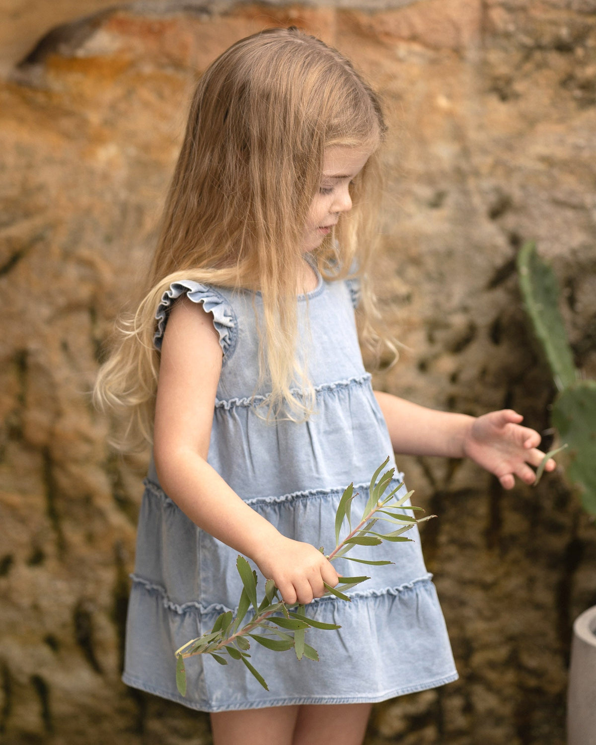 Child with long fair hair in the Indiana tiered dress, holding a leafy sprig