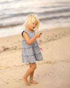 Child on the beach in the Indiana tiered dress, looking at a pebble in her hand