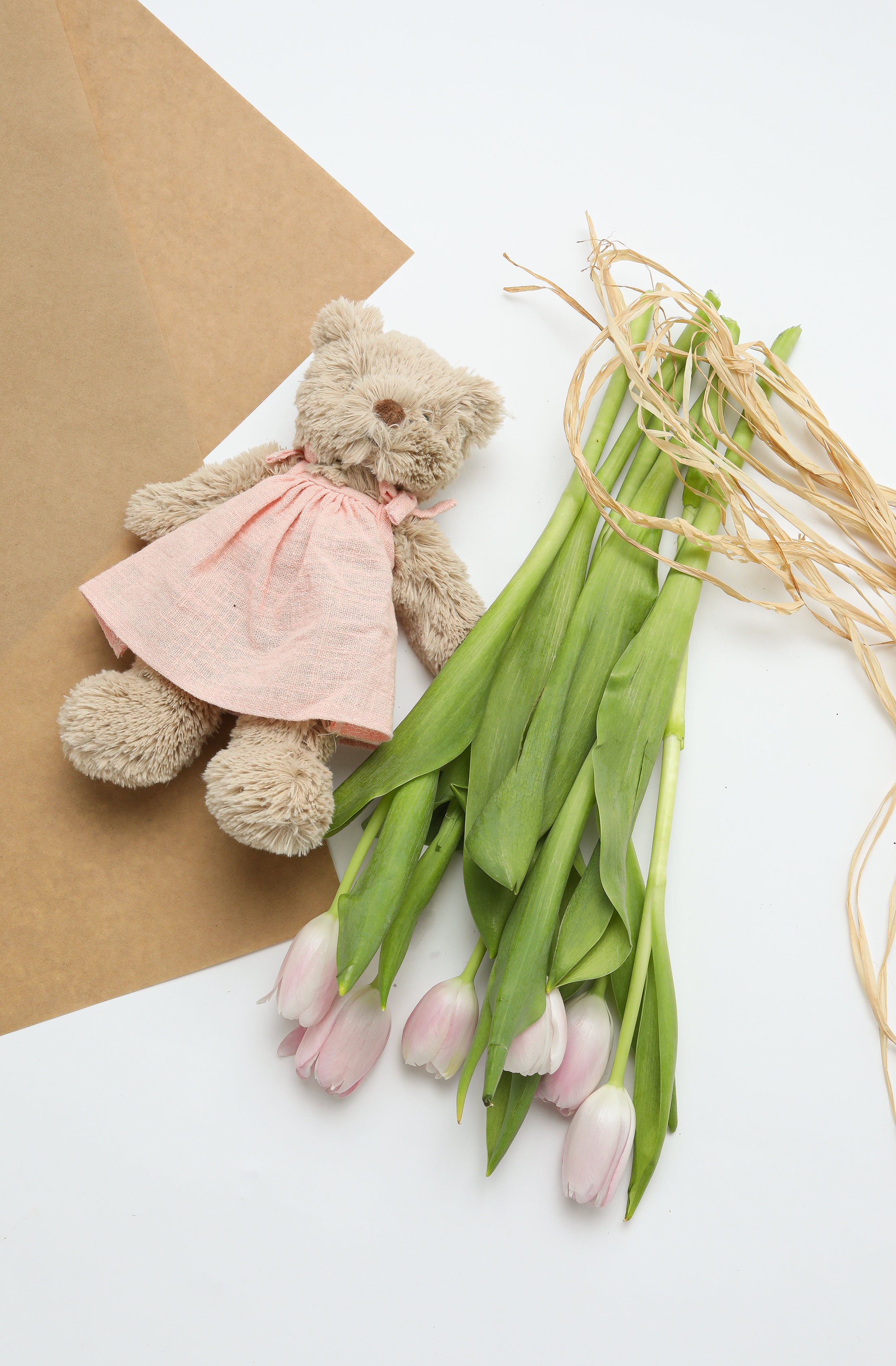 The bear lying on brown paper beside a bunch of pink tulips tied with raffia.