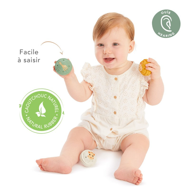 Baby in a white outfit holding the green and yellow balls, with easy-to-grasp and natural rubber badges captioned around them.