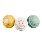 Three Sophie la Girafe musical balls in mustard yellow, white and sage green, each embossed with Sophie's face or a giraffe motif.