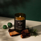 Lit Barber Shop candle in an amber reclaimed wine bottle beside pine cones and timber