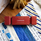 Red Cherish bath salt bon bon, shaped like a Christmas cracker, on a patchwork quilt.