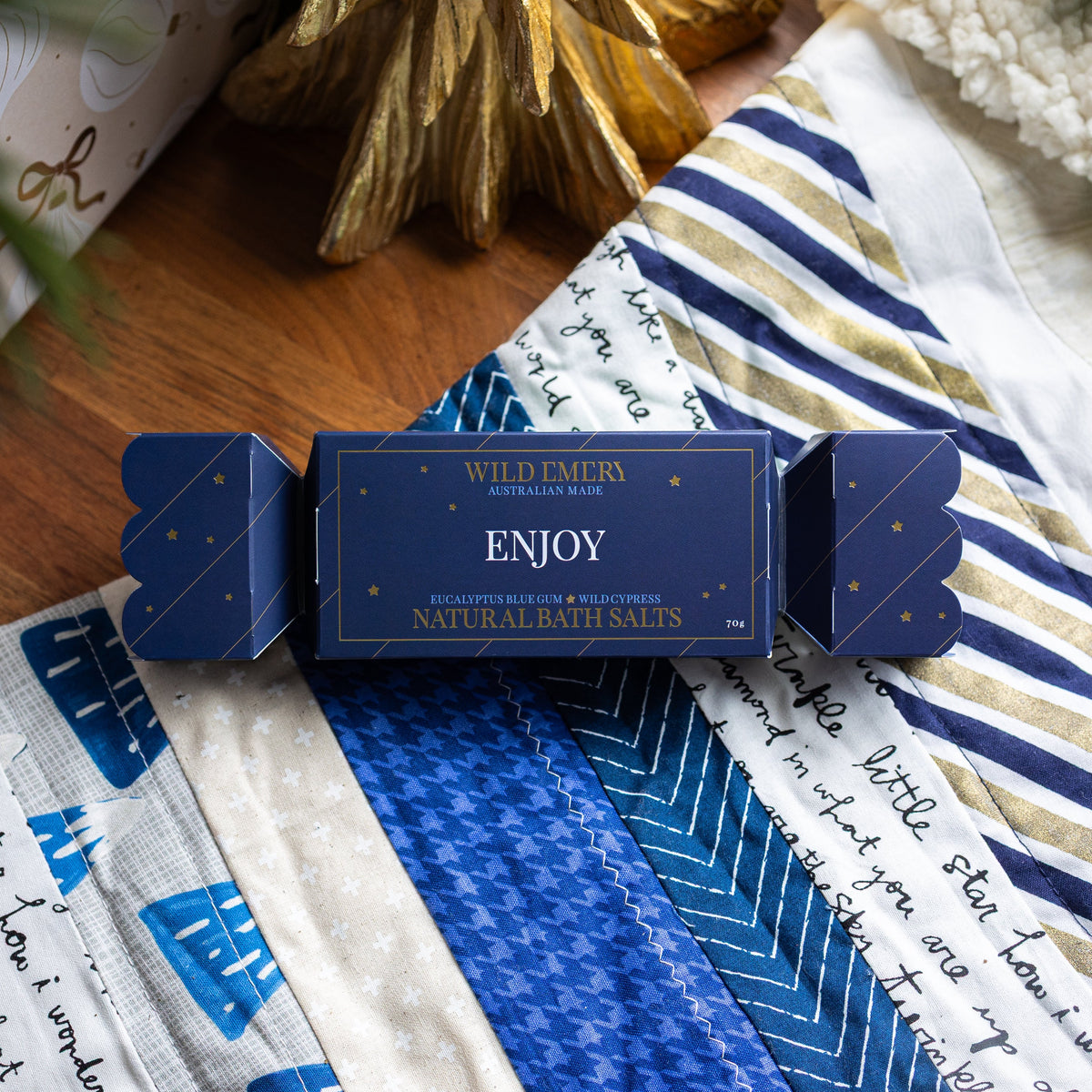 Navy Enjoy bath salt bon bon, shaped like a Christmas cracker, on a patchwork quilt.