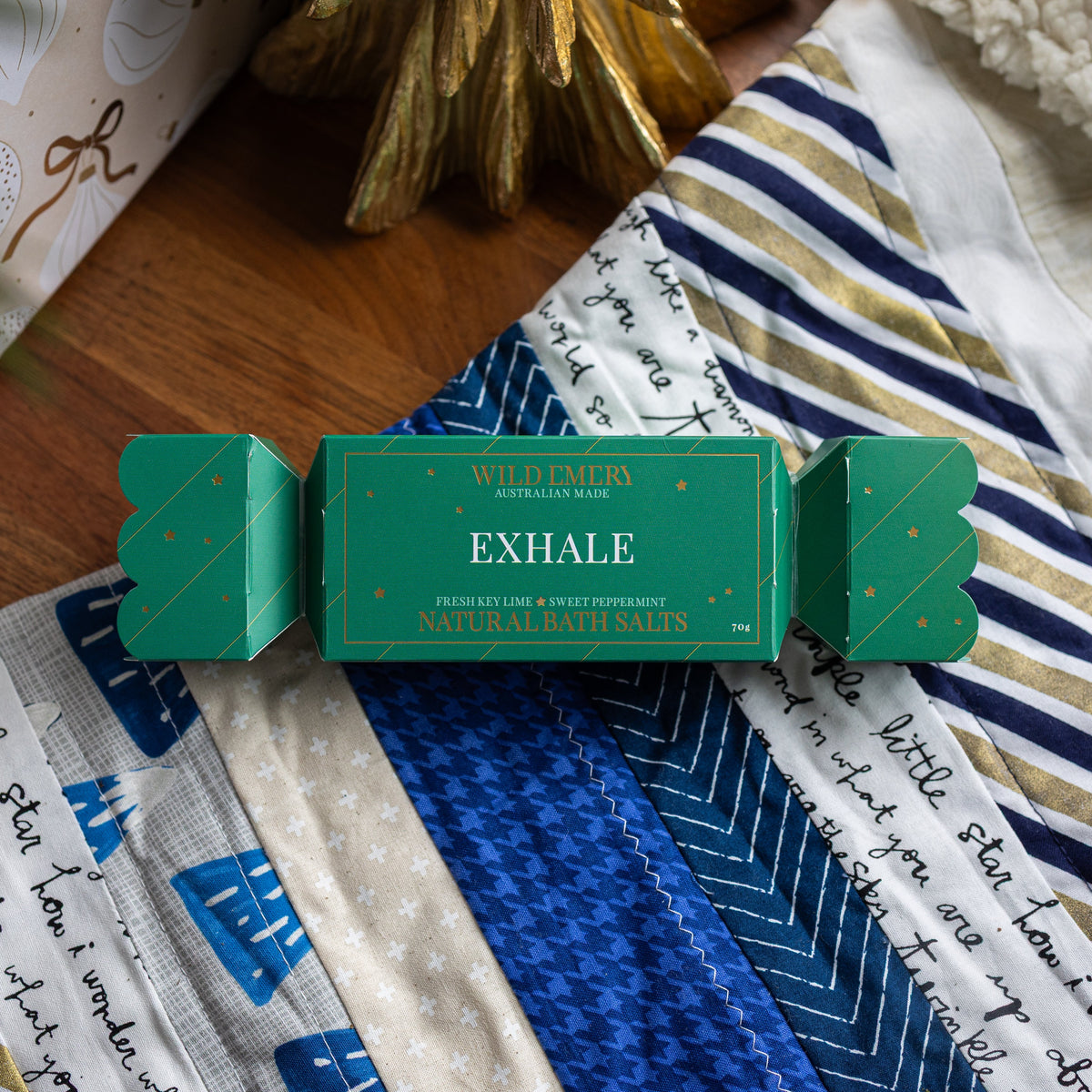 Emerald green Exhale bath salt bon bon, shaped like a Christmas cracker, on a patchwork quilt.