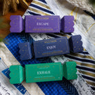 The three bon bons from the set, purple Escape, navy Enjoy and green Exhale, on a patchwork quilt.