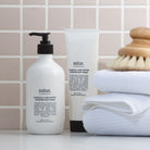 Salus Calendula & Shea Butter body cream pump bottle and tube on a tiled shelf with towels and a body brush