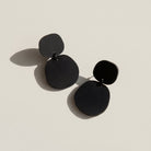 A pair of matte black acrylic dangle earrings, each a small rounded pebble shape above a larger one.