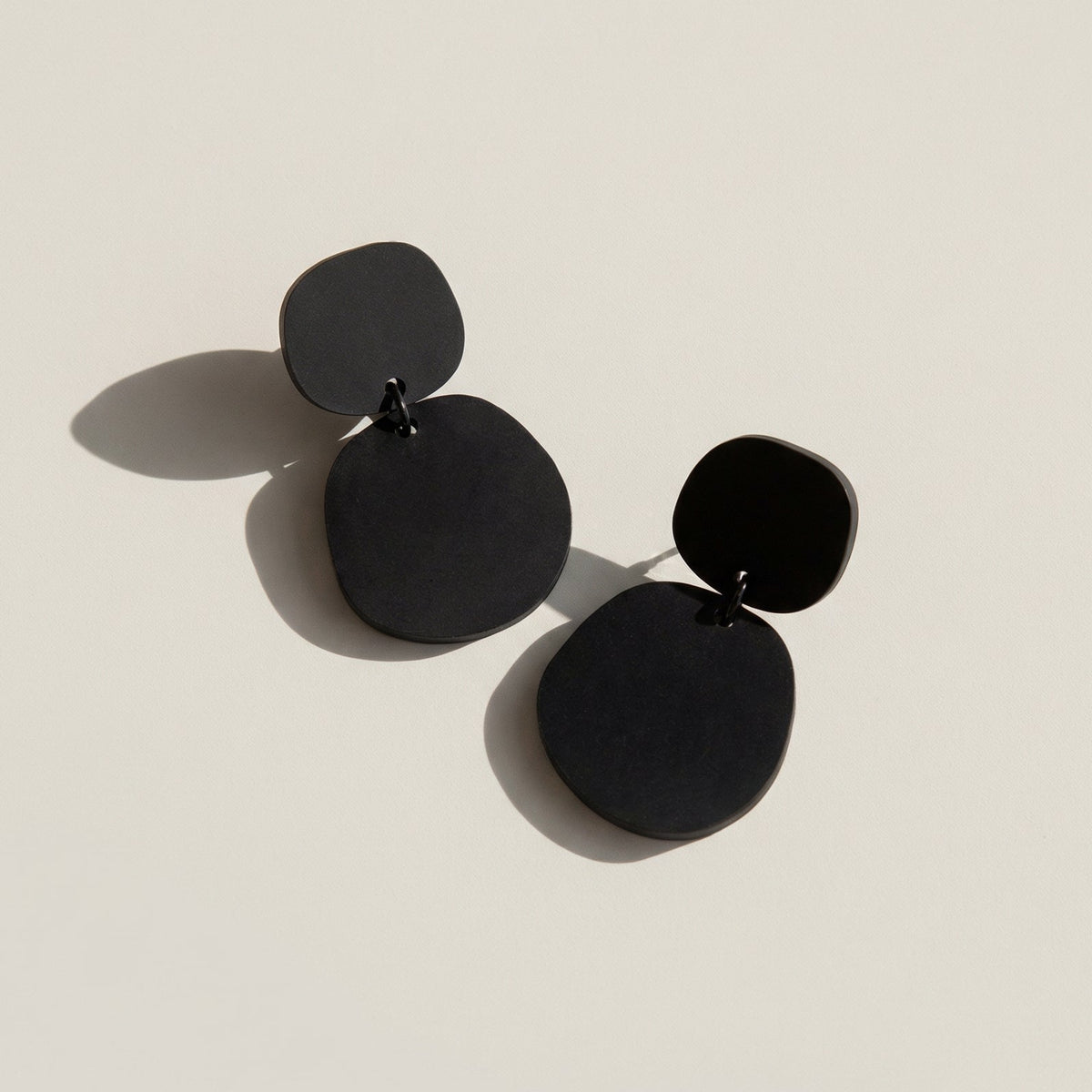 A pair of matte black acrylic dangle earrings, each a small rounded pebble shape above a larger one.