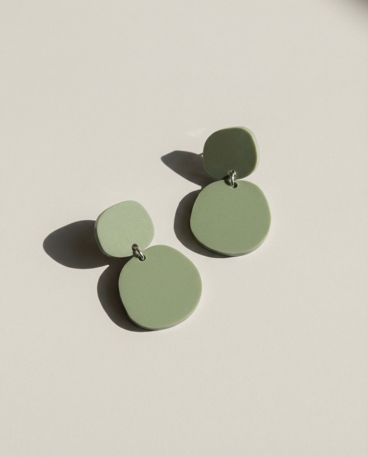 A pair of olive green acrylic dangle earrings, each a small rounded pebble shape above a larger one.