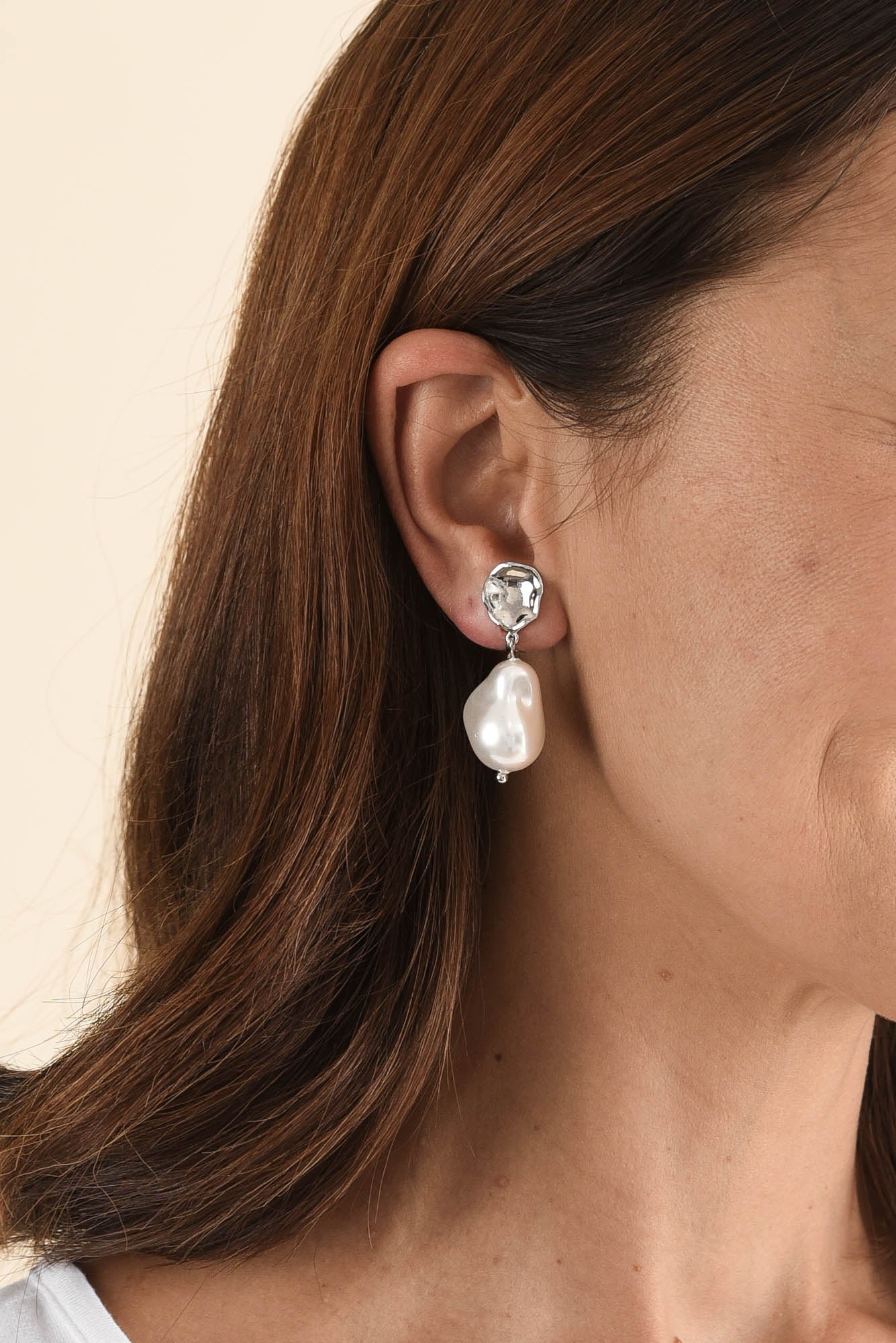 A Calais clip-on earring worn: a hammered silver-tone top with a baroque pearl drop.