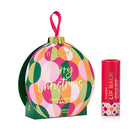 Huxter Vanilla Bean lip balm in a round bauble box patterned with green, pink and orange circles, Merry Christmas in gold, beside the red balm tube.