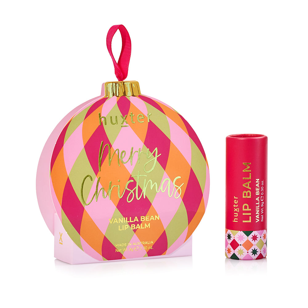 Huxter Vanilla Bean lip balm in a round bauble box with pink, orange and green diamonds, Merry Christmas in gold, beside the red balm tube.
